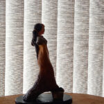 Silhueta na sombra da escultura em terracota Estrige Elegante, destacando sua forma frente a um plano de persiana vertical