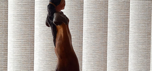 Silhueta na sombra da escultura em terracota Estrige Elegante, destacando sua forma frente a um plano de persiana vertical