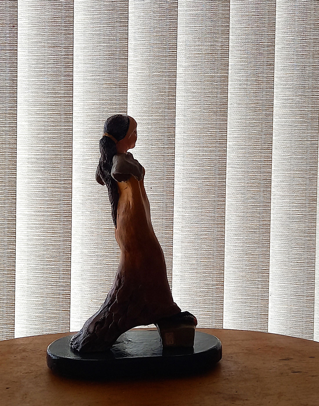 Silhueta na sombra da escultura em terracota Estrige Elegante, destacando sua forma frente a um plano de persiana vertical