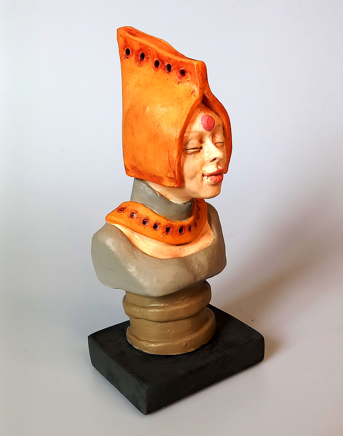 Visão da estatueta autoral em cerâmica policromada Lady Gamati Meditando com capuz de cor açafrão