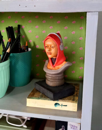 estatueta autoral Lady Gamati decorando estante com livro e elementos decorativos