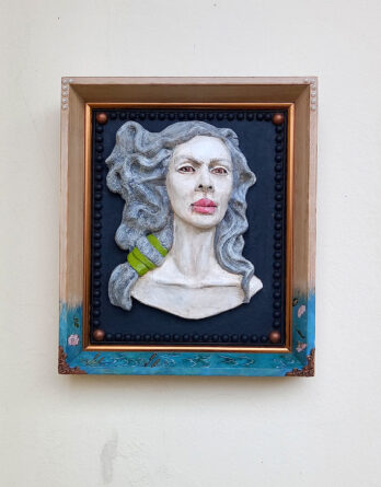 Visão frontal do relevo em cerâmica Vento de Afrodite fixado em moldura com detalhes de pintura na base em fundo branco