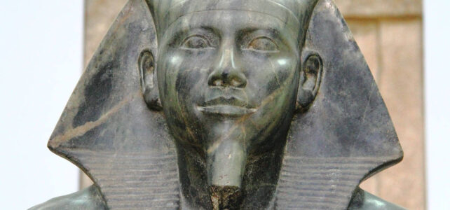 Close-up frontal do rosto do faraó Quéfren com o lenço real Nemés, exibindo uma expressão solene e barba postiça entalhada.