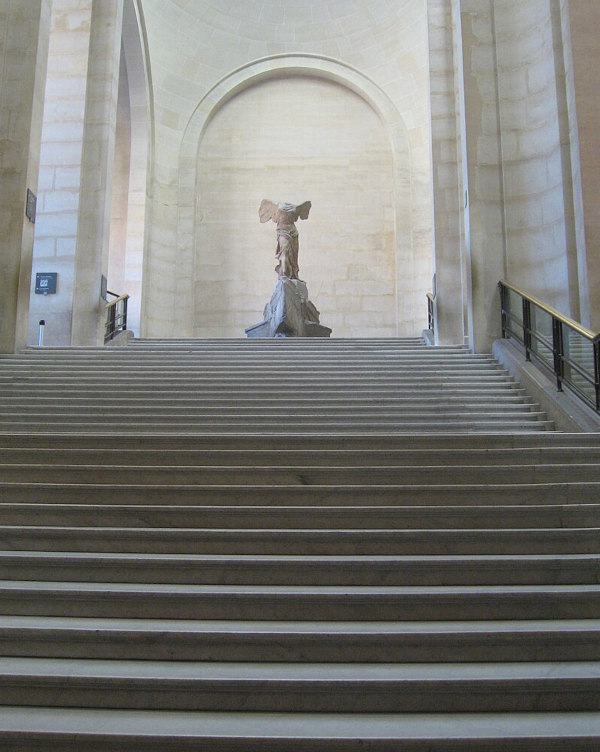Vista imponente da Vitória de Samotrácia no topo das escadarias Daru no Museu do Louvre