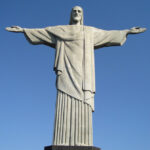 Vista completa da estátua do Cristo Redentor no topo do Corcovado com os braços abertos sob céu limpo.
