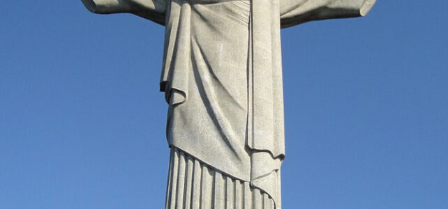 Vista completa da estátua do Cristo Redentor no topo do Corcovado com os braços abertos sob céu limpo.