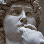 Close-up do rosto da estátua David de Michelangelo focado na expressão intensa e decidida do olhar direcionado para o lado