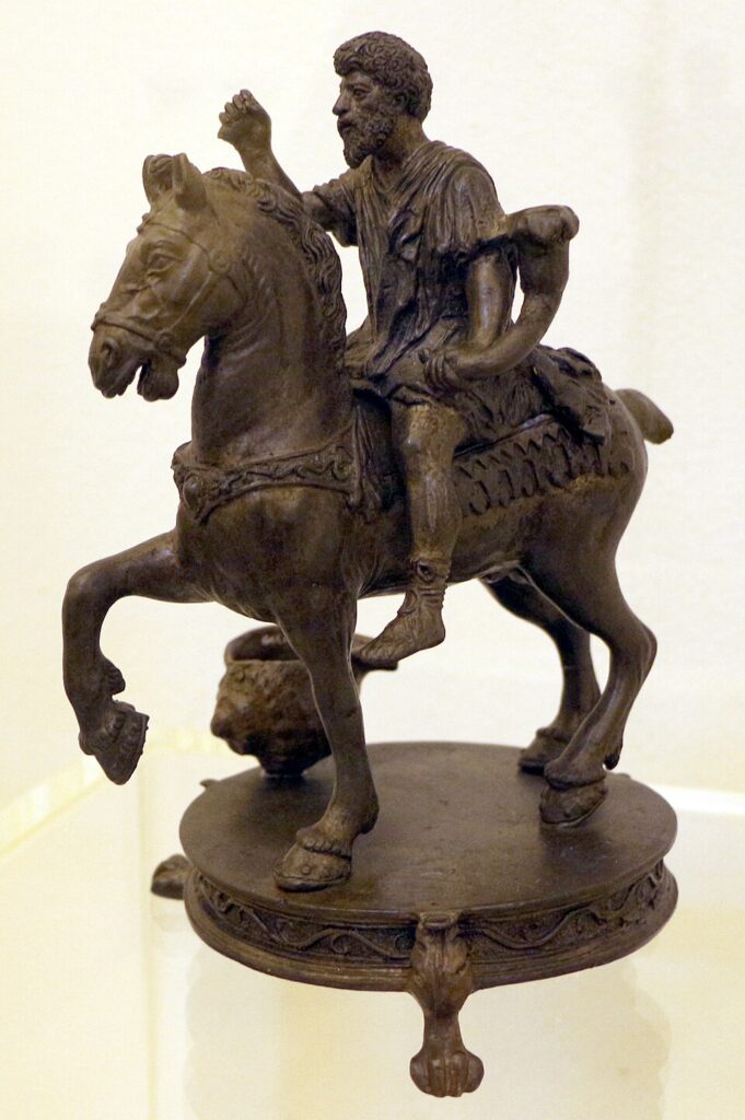 Estatueta em bronze escuro de um rei a cavalo sobre um pequeno pedestal