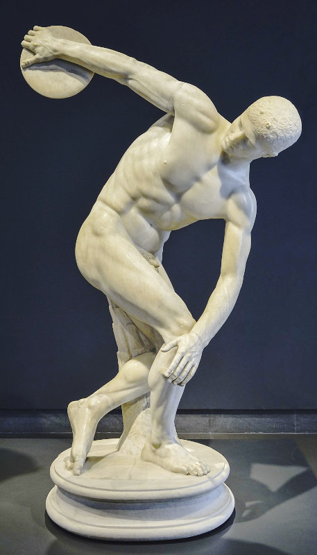 imagem de uma escultura romana em mármore branco de um atleta nu no momento que vai lançar um disco, em um museu