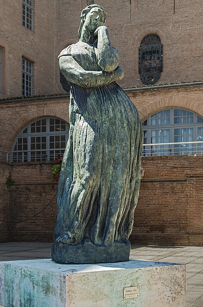estátua de bronze esverdeado de uma mulher com vestido longo em posição em pé parecendo que está em espera