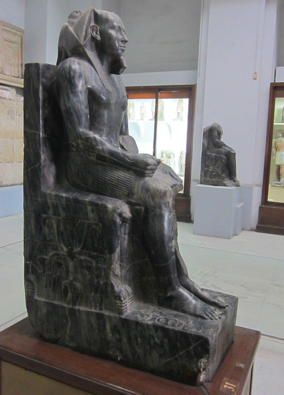 estátua em pedra escura de um faraó sentado no trono no espaço de um museu de arte egípcia