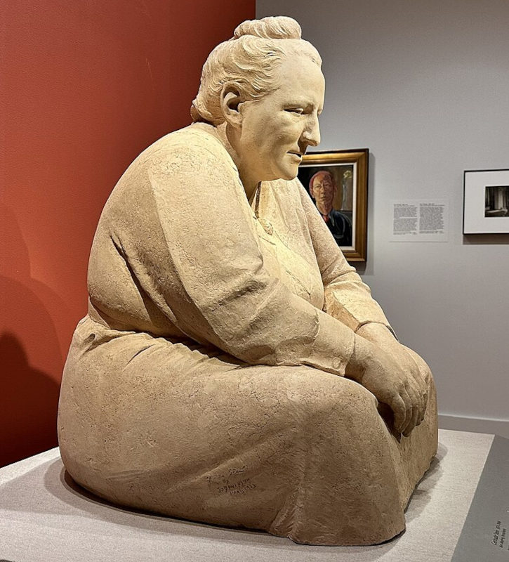 escultura em argila de uma senhora sentada com ar reflexivo apoiada sobre uma base em um museu