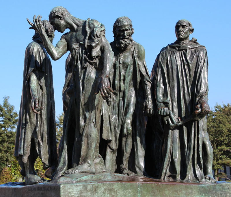 Escultura em bronze escuro de seis homens com expressões angustiadas vestidos com panos longos, em uma praça