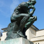 escultura em bronze O Pensador sobre o tumulo de Rodin frente a um céu azul
