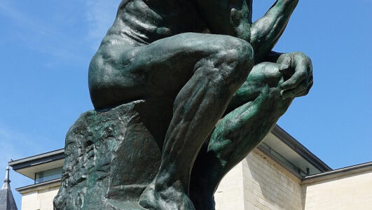 escultura em bronze O Pensador sobre o tumulo de Rodin frente a um céu azul