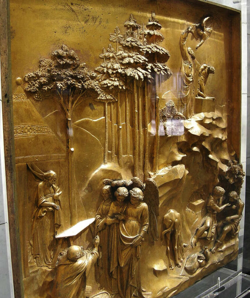 foto aproximada de um relevo em metal dourado com motivo religioso e elementos decorativos ao fundo