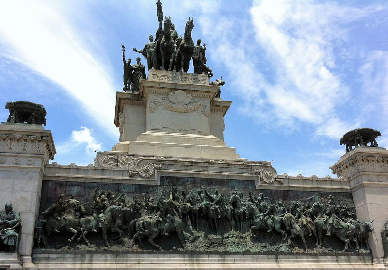 relevos de uma batalha da época da independencia do Brasil, com soldados a cavalo e vista do monumento do ipiranga sobre um cécu azulado