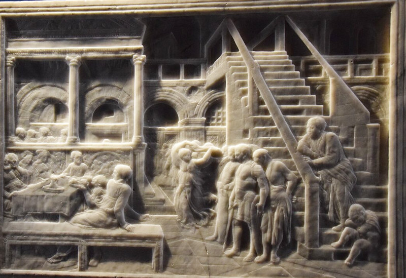 relevo em mármore da cena de um banquete com várias figuras ao redor de uma mesa e escadarias e parte da construção