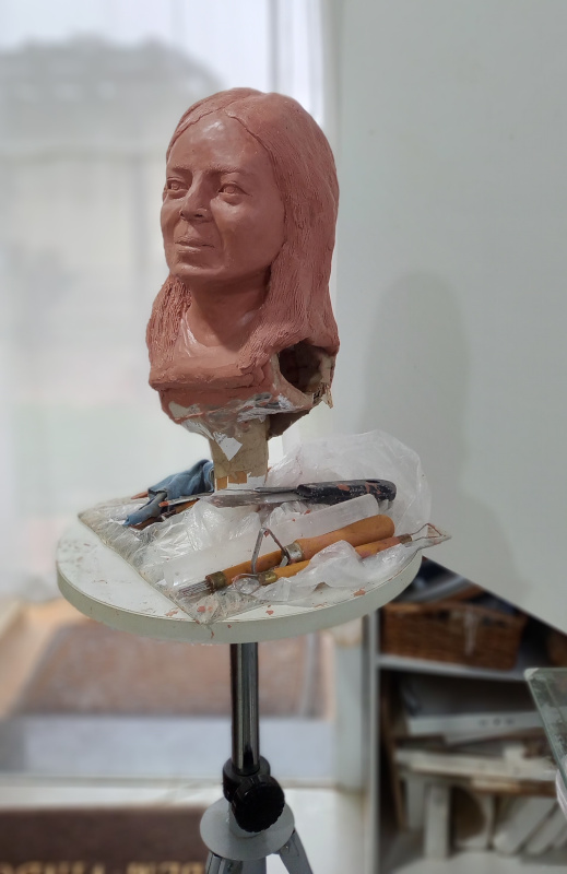 ateliê de escultura destaque uma cabeça de mulher em argila sobre um cavalete de escultor com algumas ferramentas