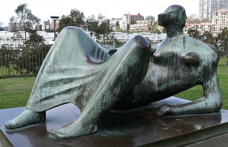 estátua de uma mulher deitada ao ar livre e ao fundo uma cidade