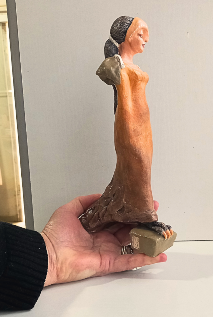 mão segurando uma estatueta de figura feminina feita em cerâmica