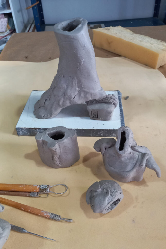 uma escultura em argila de figura feminina cortada em vários pedaços em uma bancada de ateliê