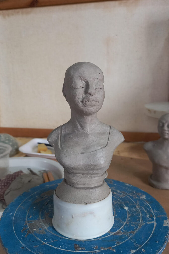 estatueta inacabada em argila de um busto de mulher na bancada de um ateliê